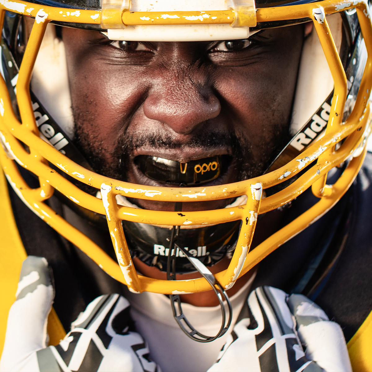 Close-up of an American football player wearing a yellow Riddell helmet and matching yellow jersey, with white gloves and a focused expression.