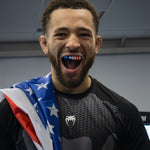 A UFC figher with a US flag draped on his shoulder wearing the OPRO Instant Custom-fit Stars and Stripes mouthguard.