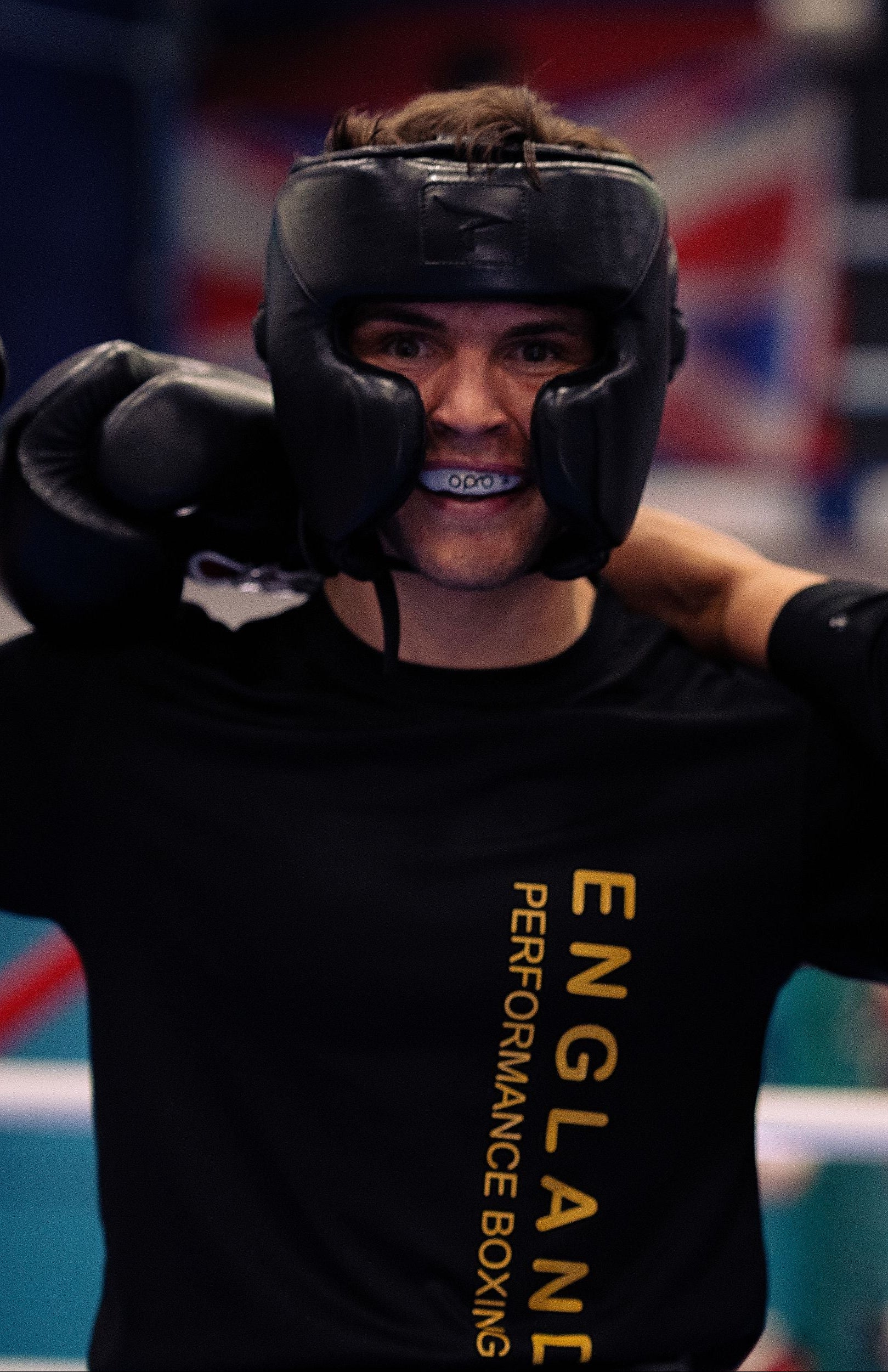 Two boxers in black 'England Performance Boxing' shirts and gear in a boxing ring.
