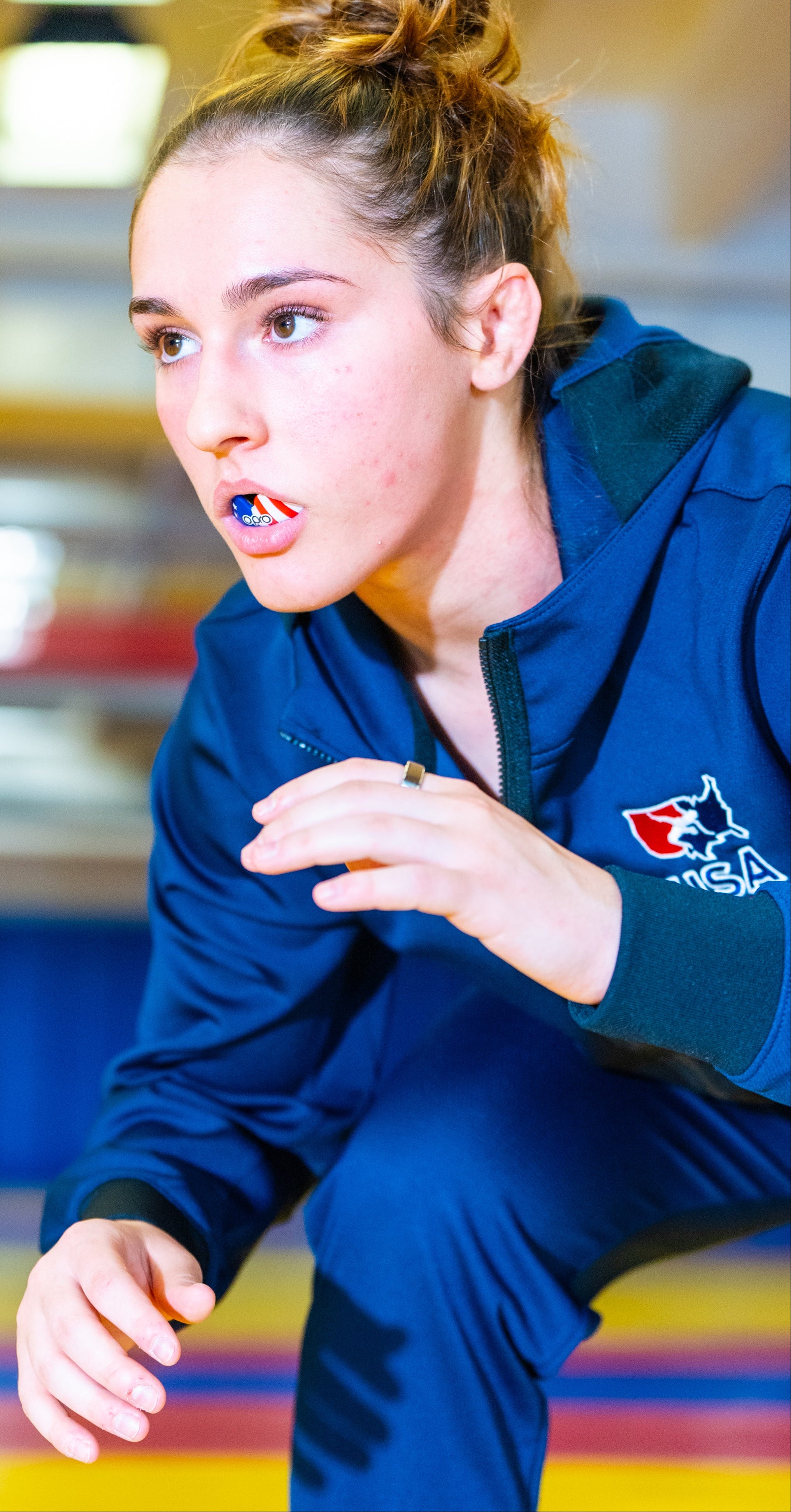 A woman in a navy blue athletic tracksuit with a wolf logo on the sleeve, crouching in a sports hall with a blurred background.