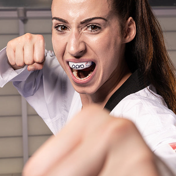 Woman in a martial arts uniform with a determined expression, ready to punch.